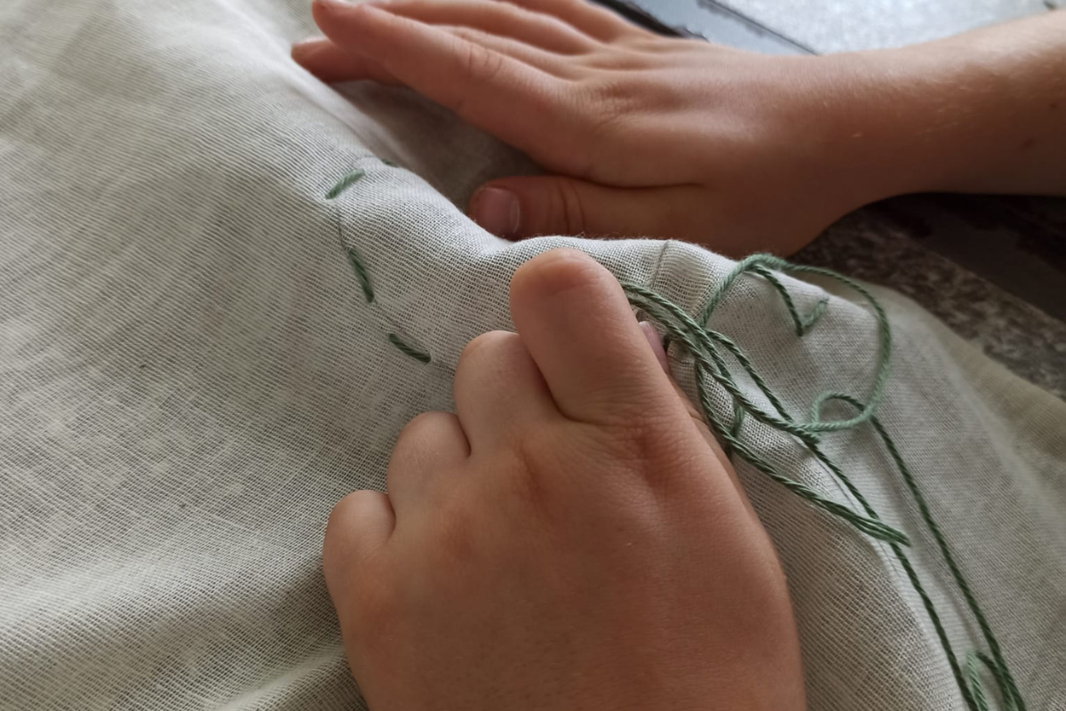 Young people's hands doing embroidery on beige linen