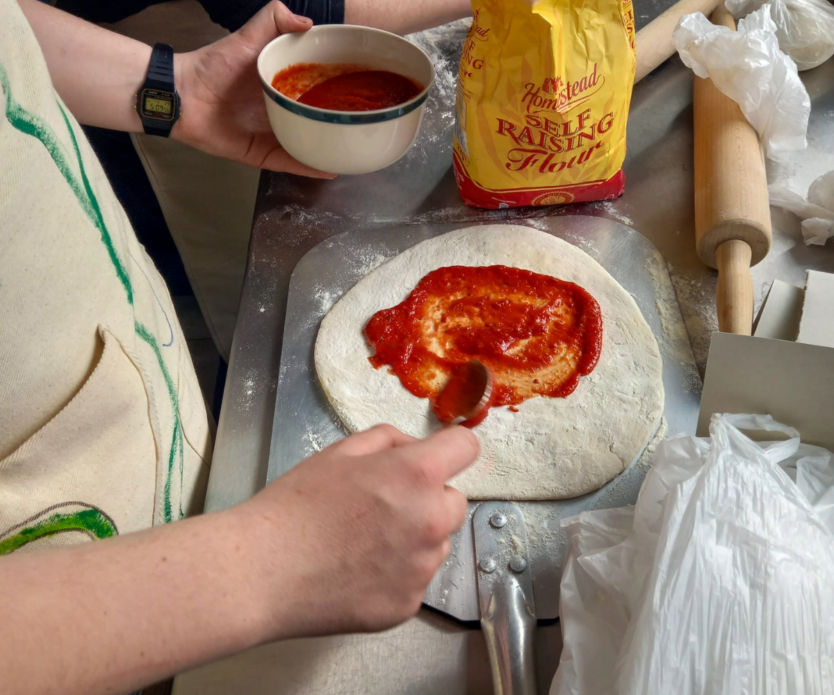 Hands spreading sauce on pizza dough